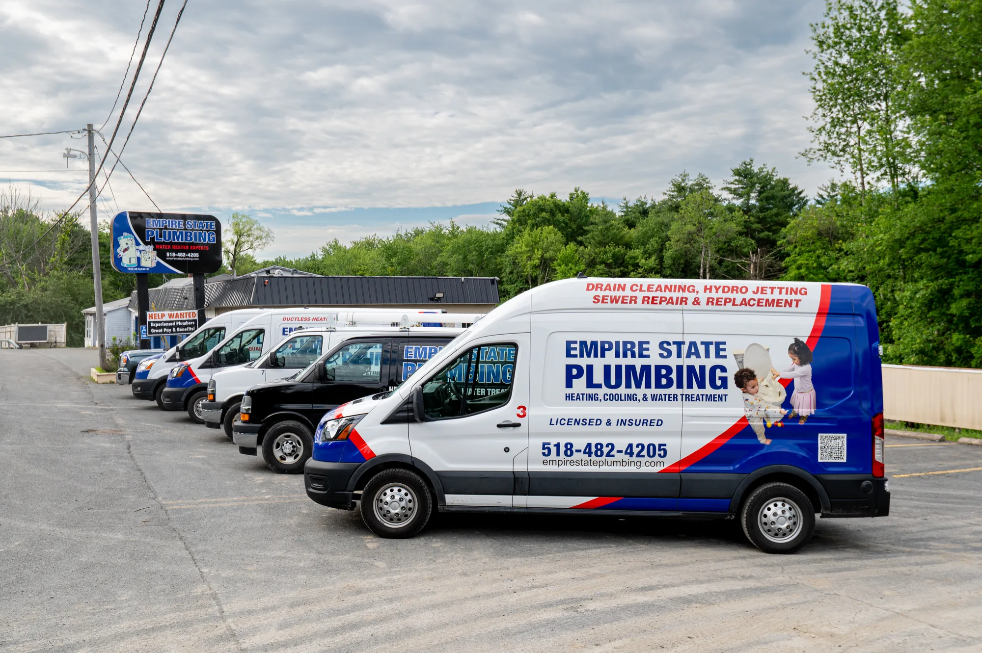 A row of Empire State Plumbing service vans lined up at the company's Nassau, NY shop beneath the Empire State Plumbing sign